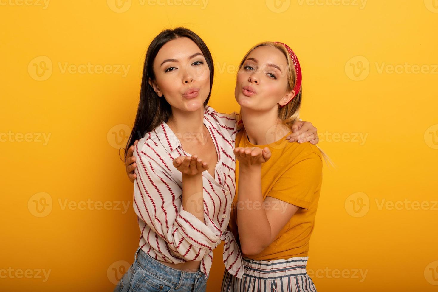 dois meninas mandar beijo para social amigos. emocional e alegre expressão. amarelo fundo foto