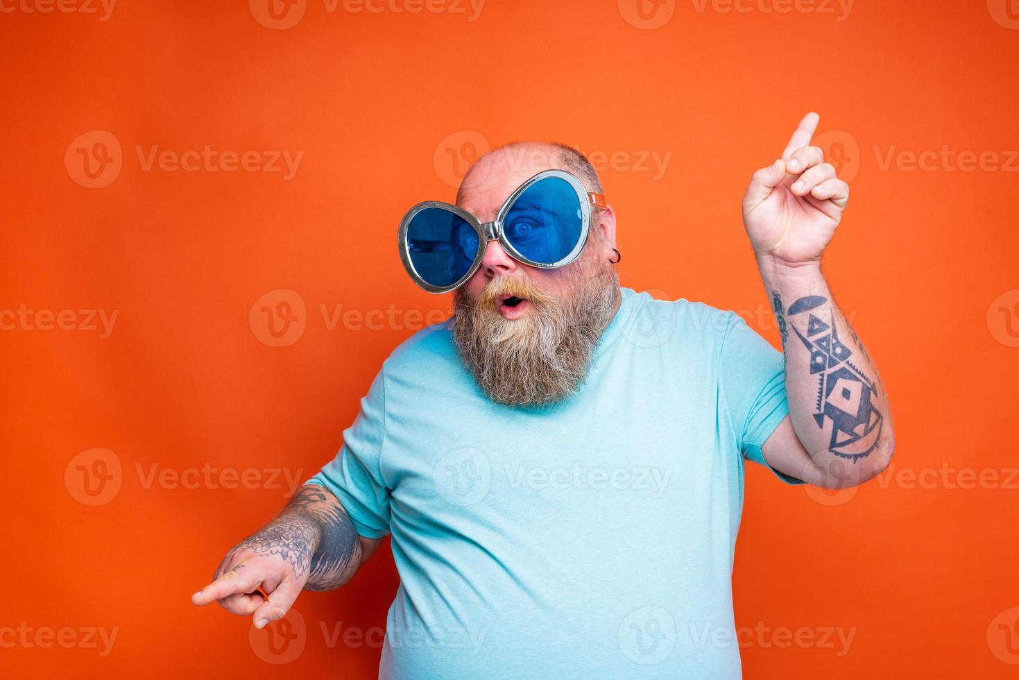 gordo espantado homem com barba, tatuagens e oculos de sol danças música foto