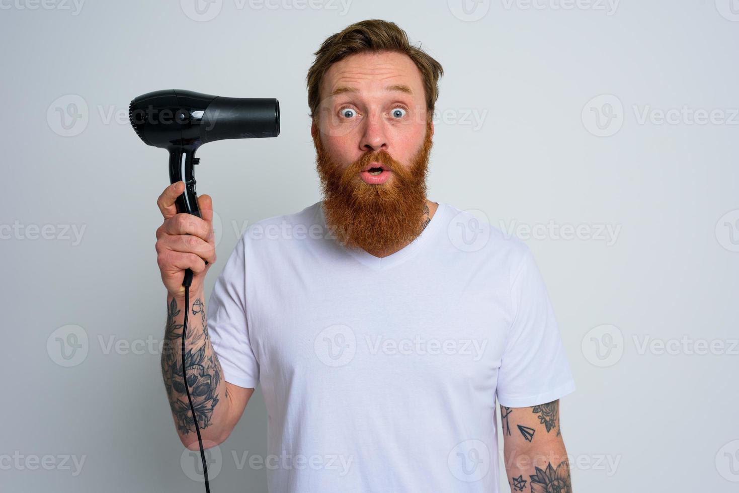 espantado homem com barba jogar com cabelo secadoras uma revólver foto