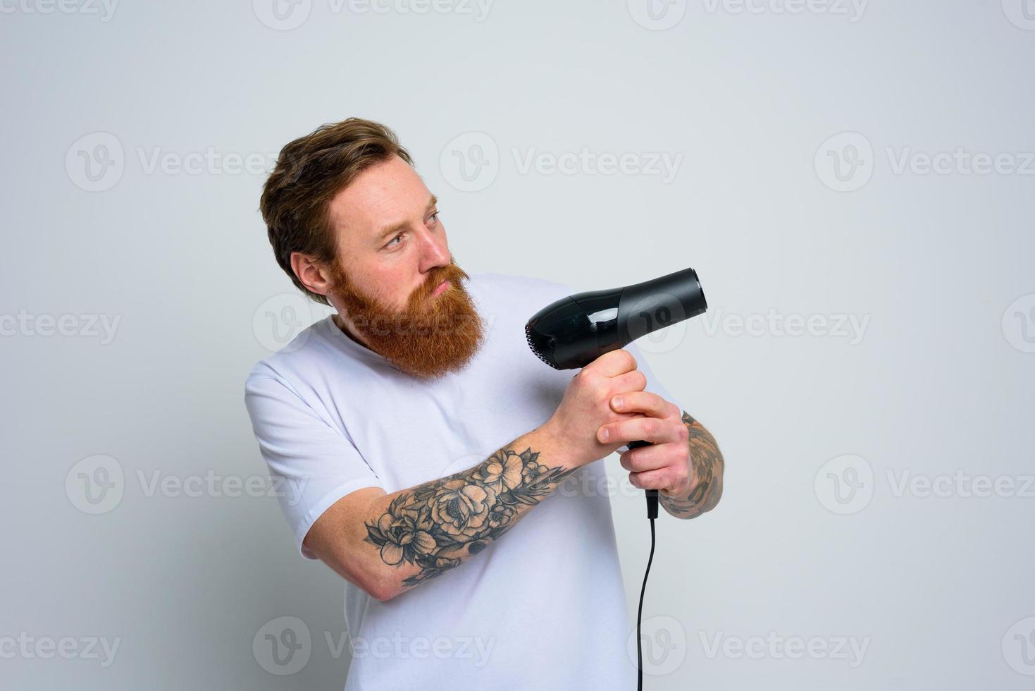 sério homem com barba jogar com cabelo secadoras uma revólver foto