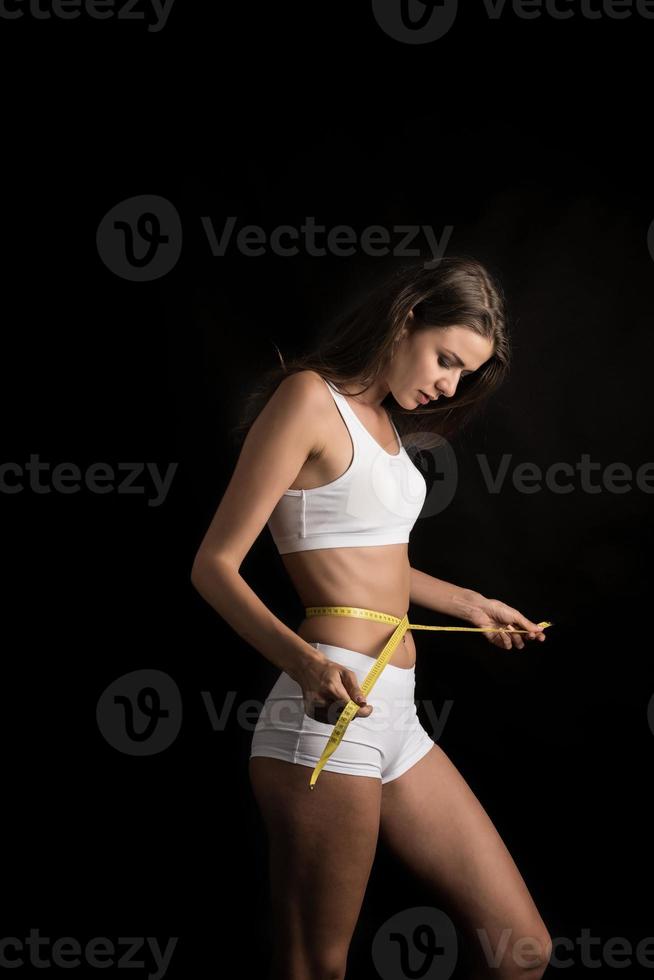 retrato de mulher jovem e bonita medindo o tamanho de seu corpo com fita métrica foto