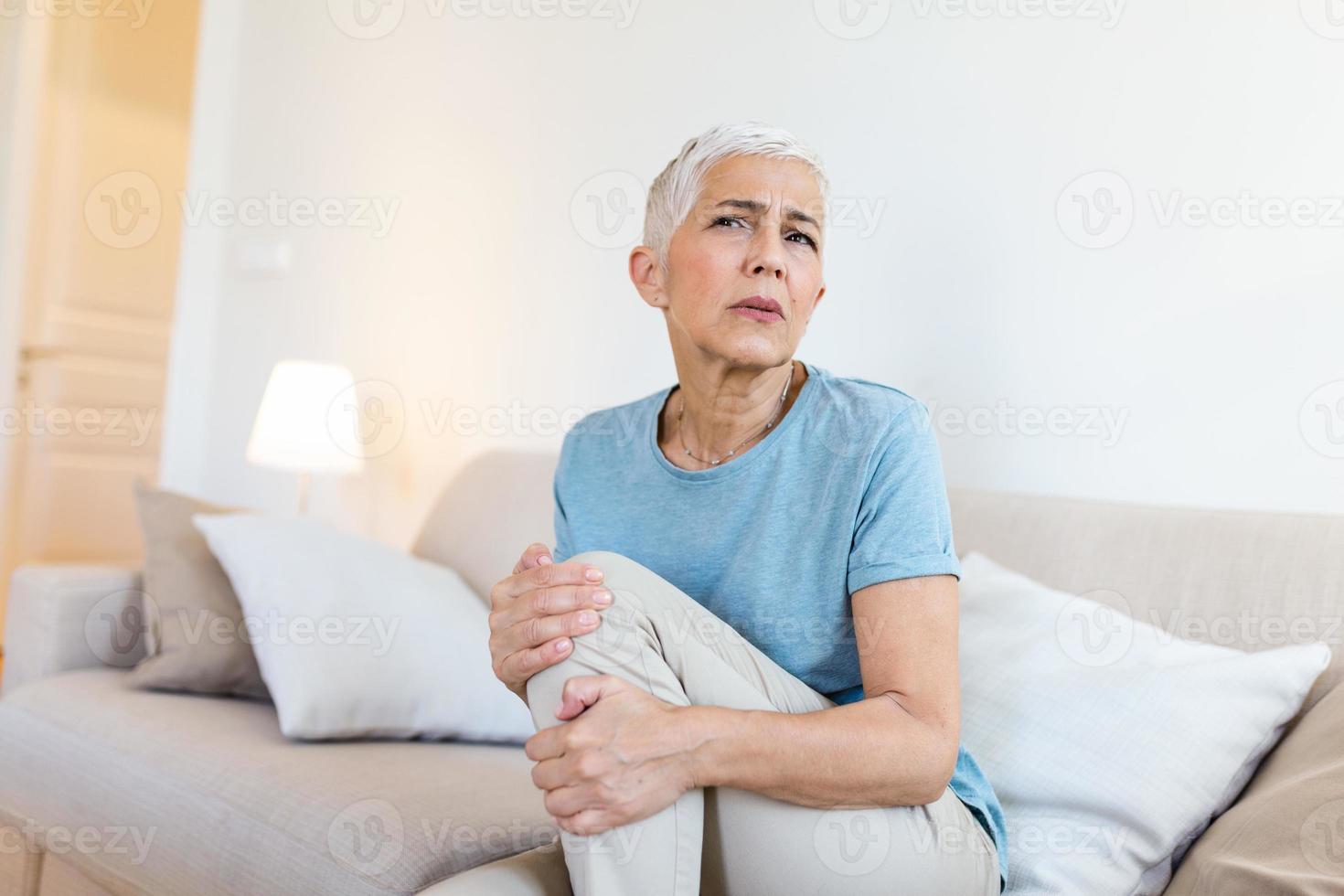 mulher sênior segurando o joelho com dor. velhice, problema de saúde e conceito de pessoas - mulher idosa que sofre de dor na perna em casa. mulher idosa que sofre de dor no joelho em casa foto