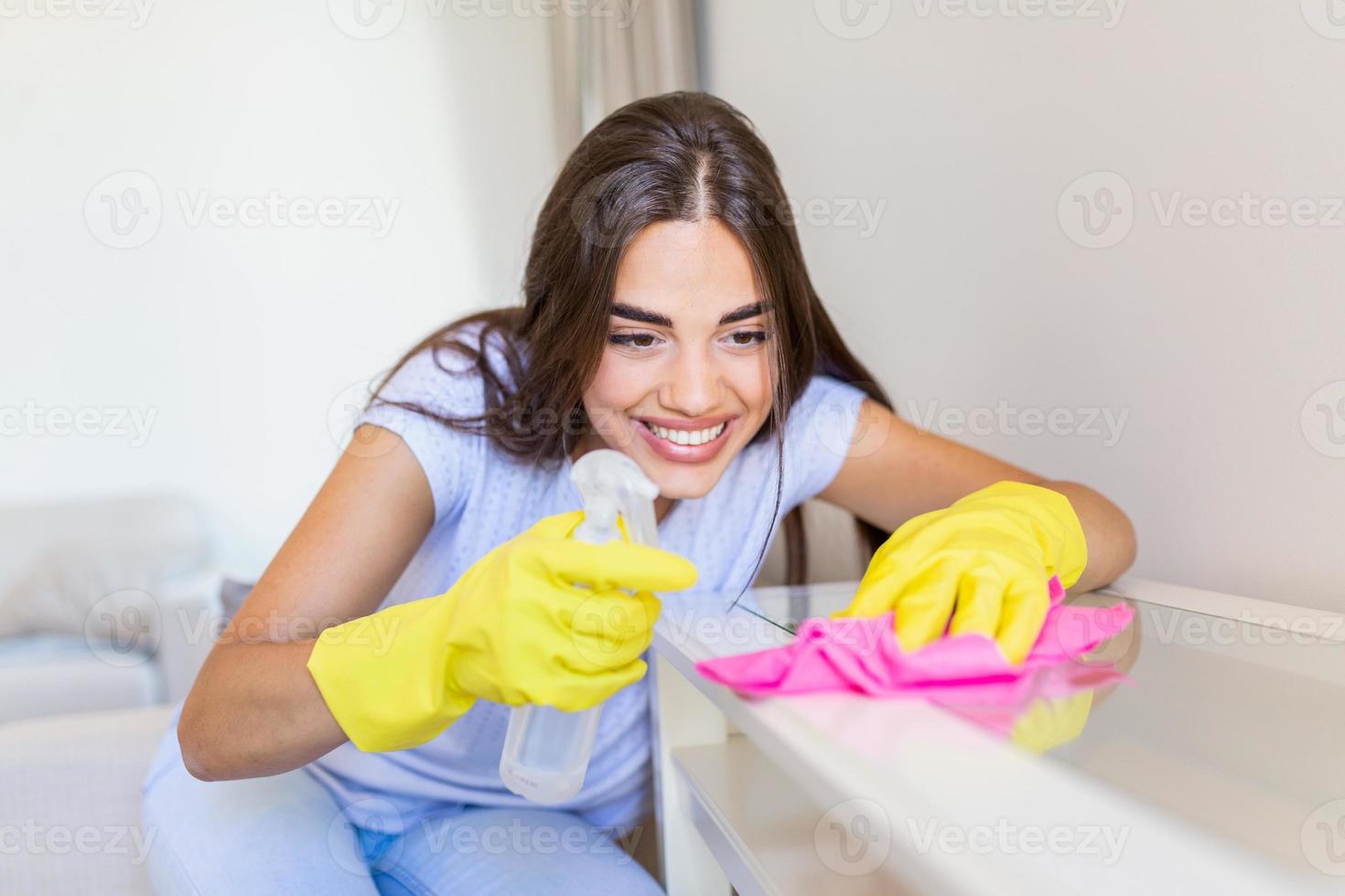 lindo jovem mulher faz limpeza a casa. menina esfrega pó. sorridente mulher vestindo borracha protetora amarelo luvas limpeza com trapo e spray garrafa detergente. lar, serviço de limpeza conceito. foto