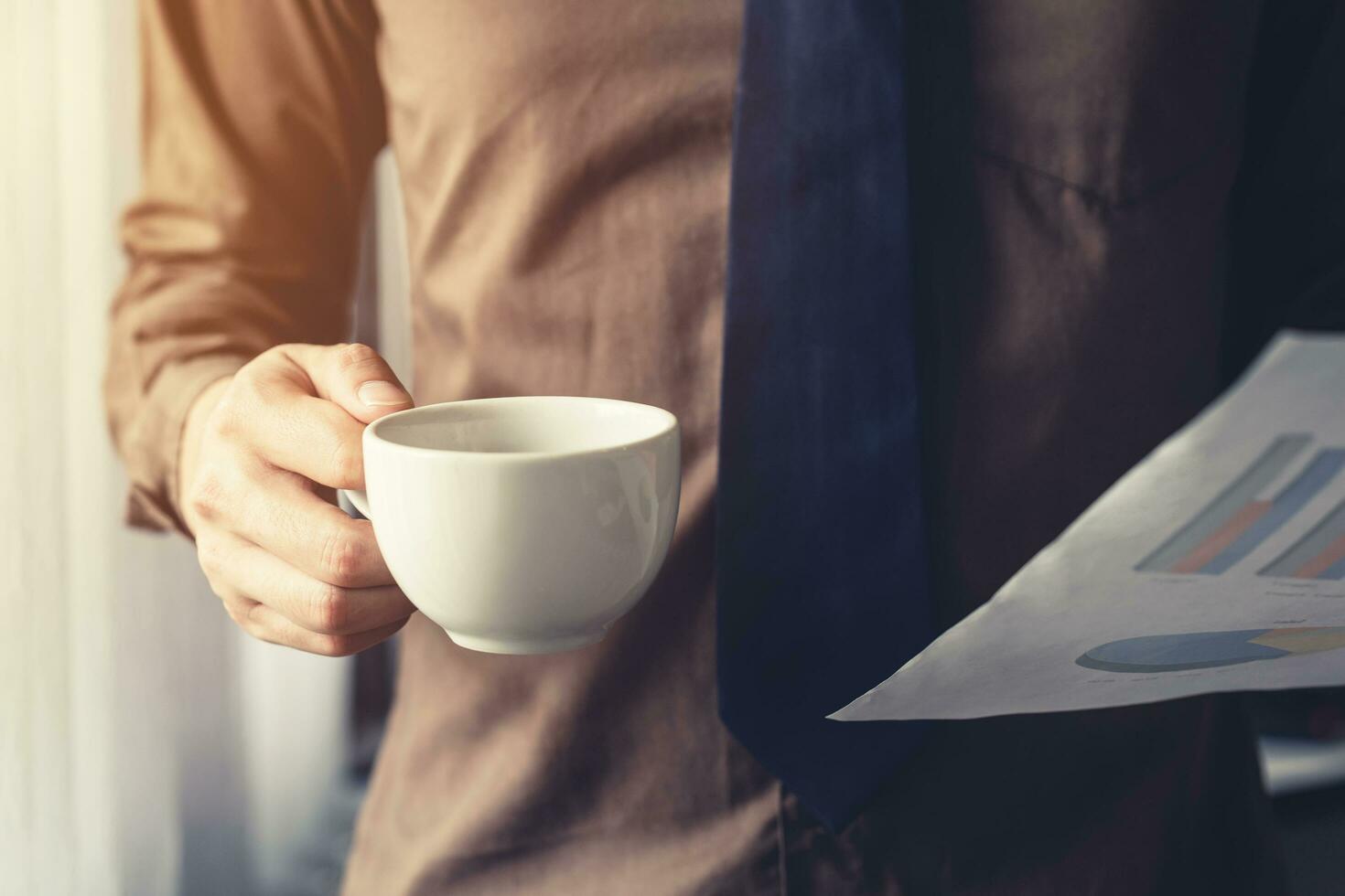 o negócio homem mão segurando café copo e papel Folha às janela dentro escritório. foto