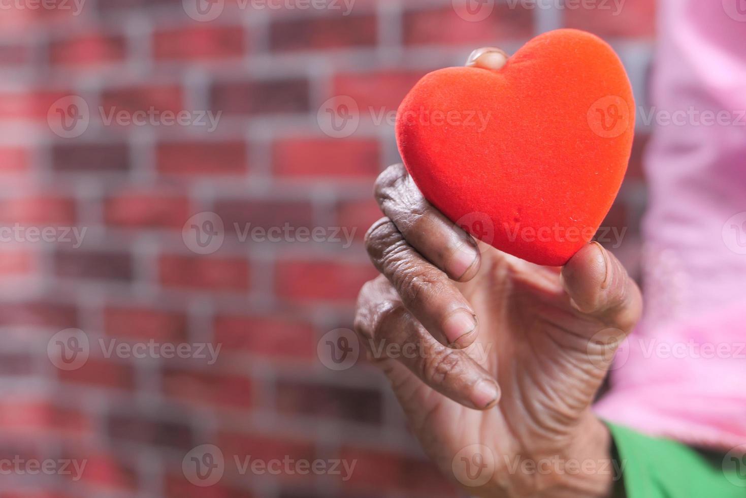 mão de uma mulher sênior segurando um coração vermelho de perto foto