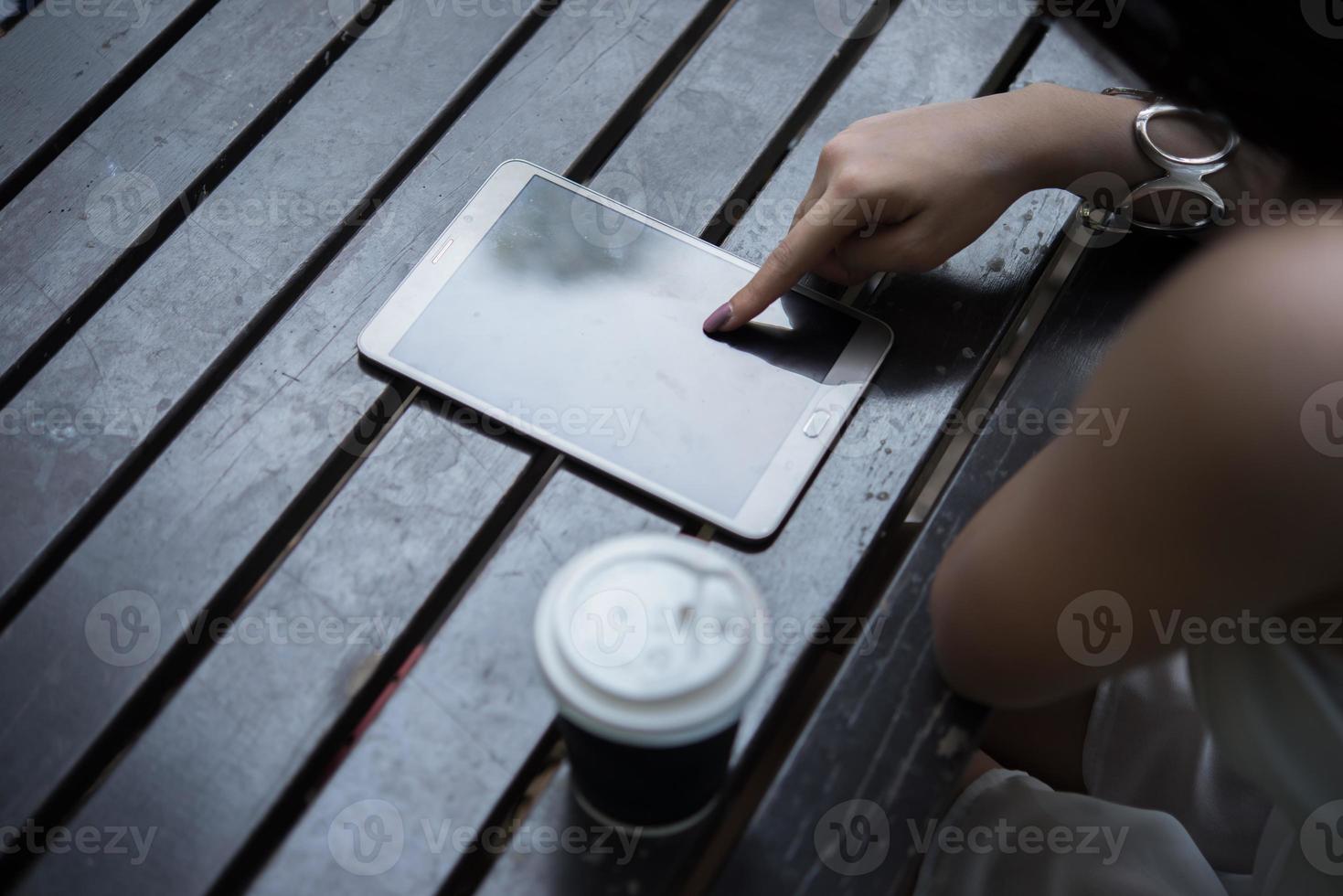 close-up de mulher segurando o computador tablet na mesa de madeira com uma xícara de café foto