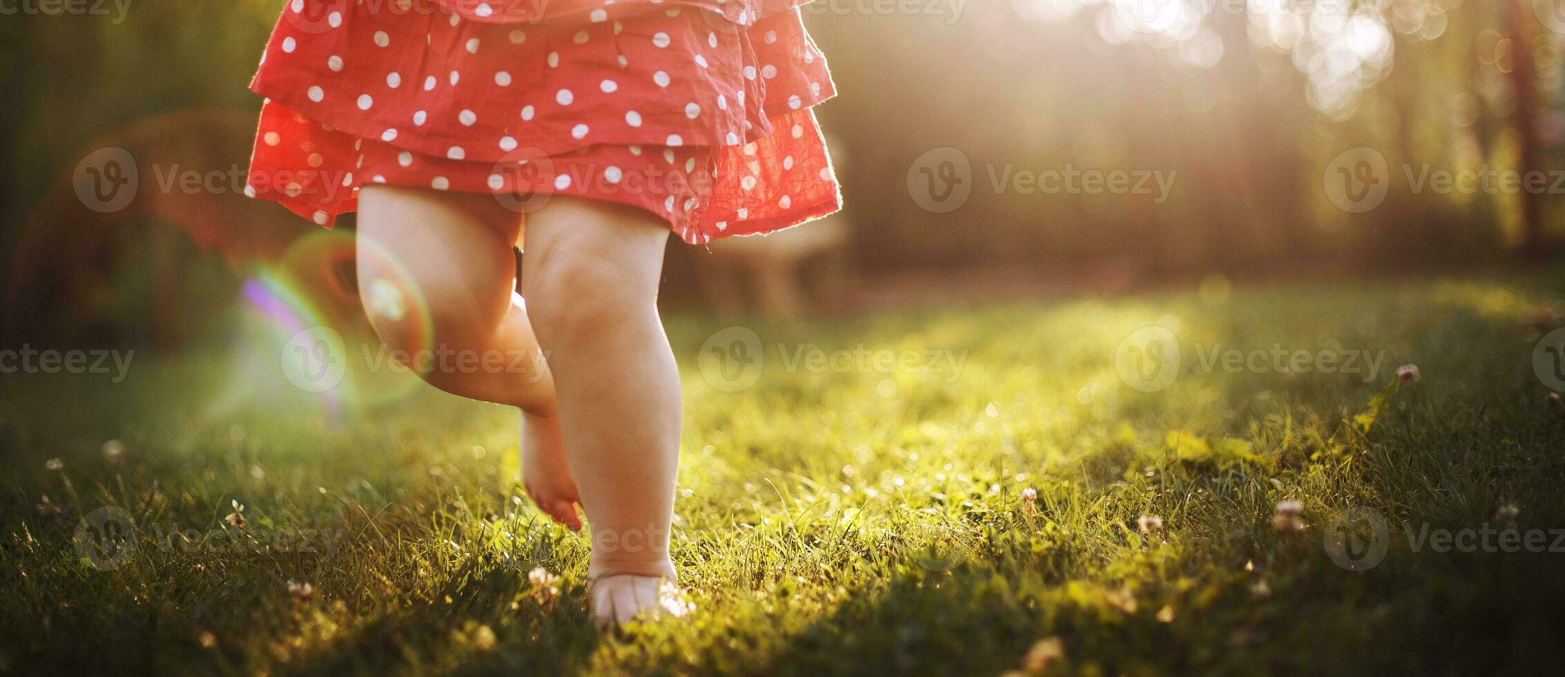 garotas nu pés dentro a verde grama. pequeno feliz criança corrida às pôr do sol descalço ar livre. foto