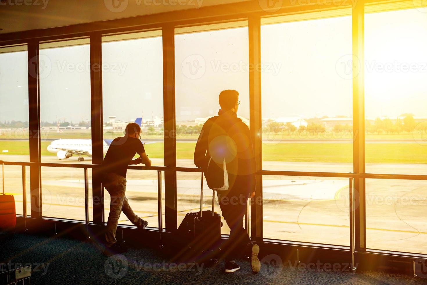 turista homens esperando para a ar avião dentro a aeroporto terminal lobby com Sol e lente flare e ar avião em corre caminho fundo. foto