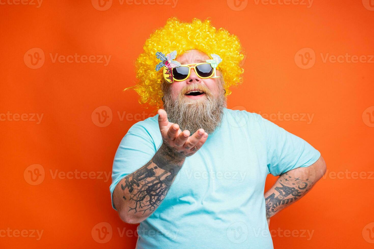 gordo feliz homem com barba, tatuagens e oculos de sol tem Diversão com a amarelo peruca foto