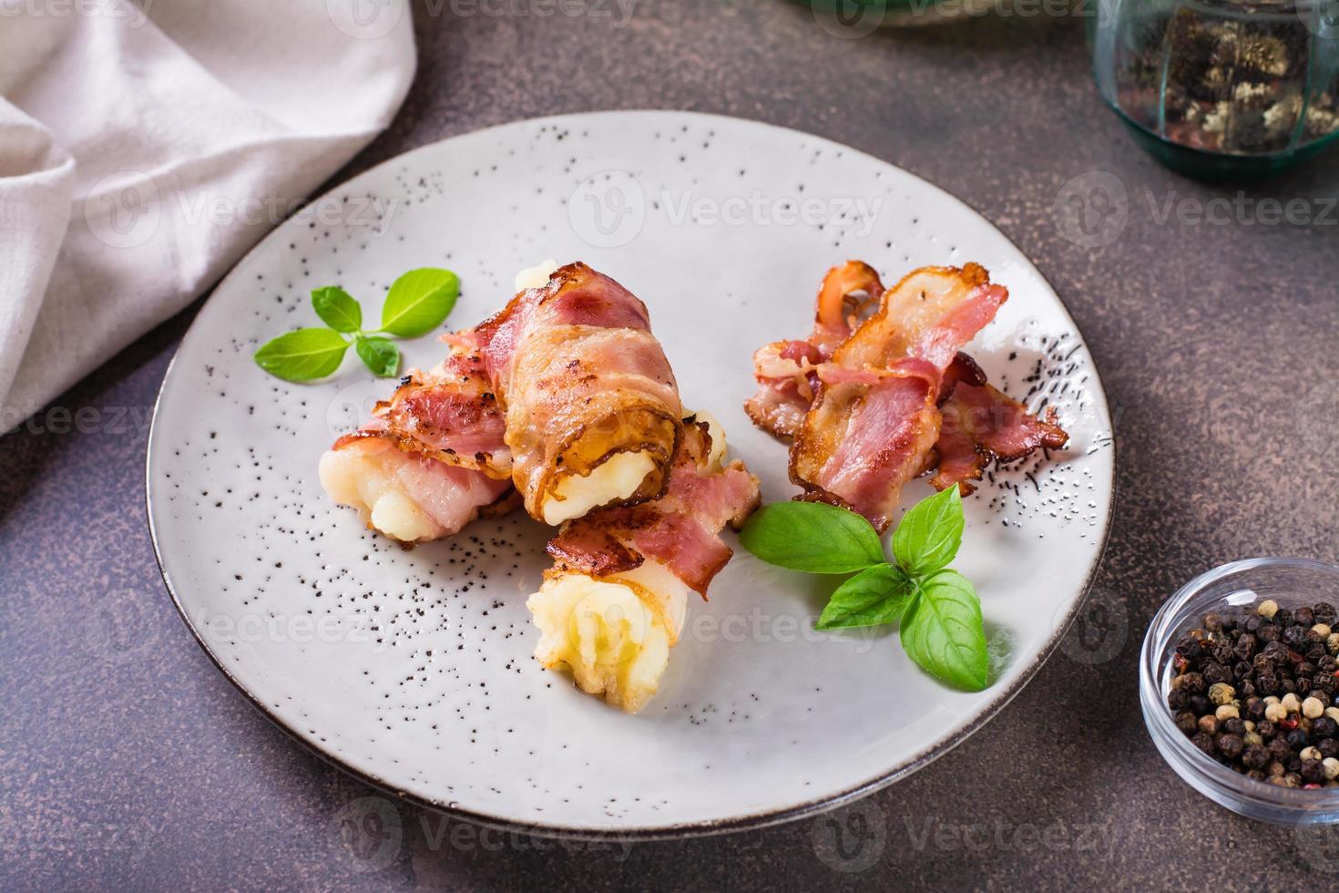 rolos do frito bacon e amassado batatas e manjericão em uma prato em a mesa. foto