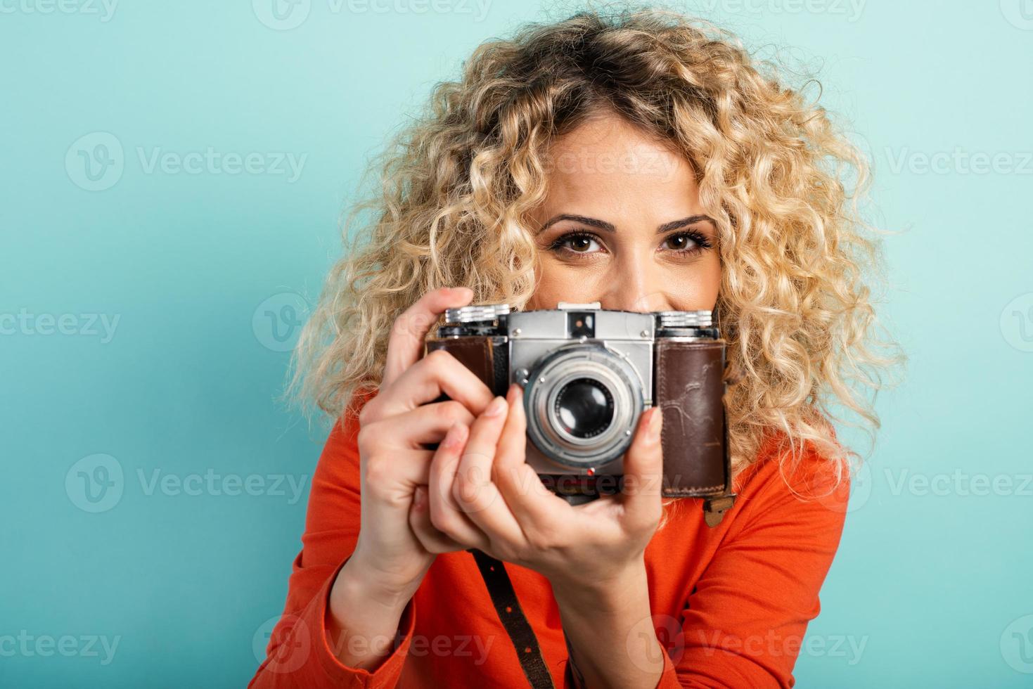 Loiras menina leva uma tiro com uma vintage fotográfico máquina. ciano fundo foto