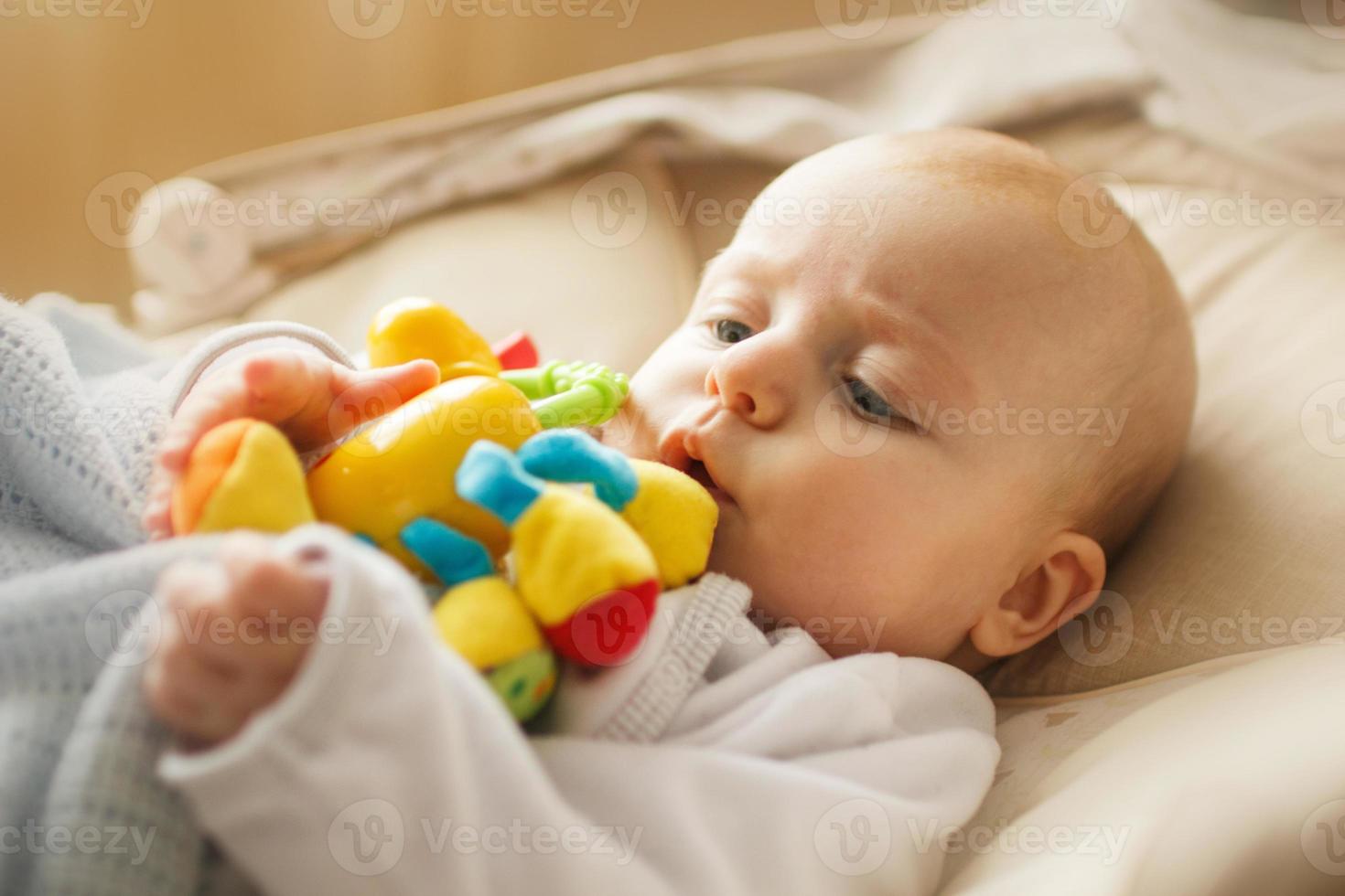 uma pequeno criança mentiras e tocam com uma brinquedo. bebê com uma brinquedo dentro dele boca foto