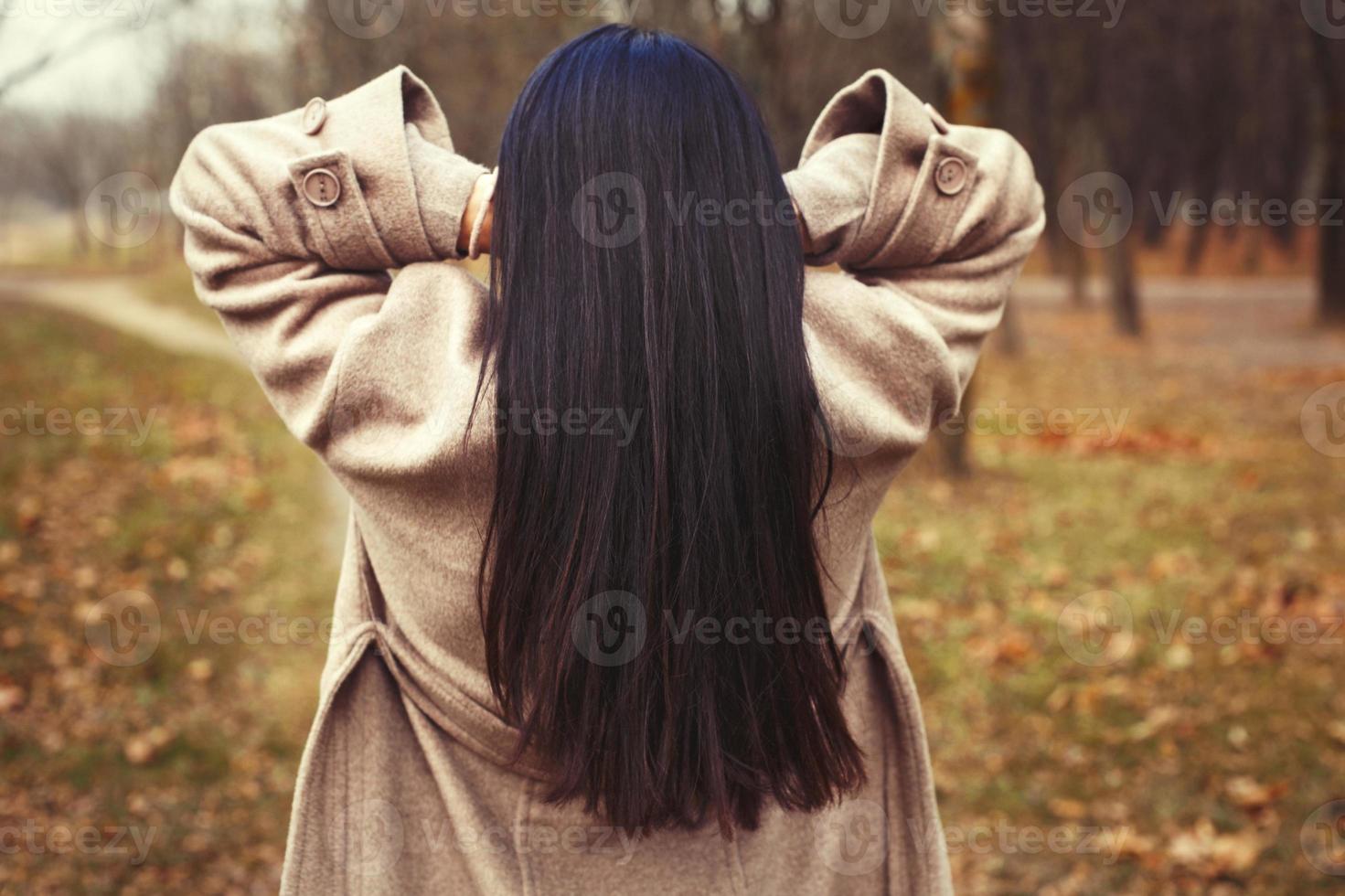 retrato do morena cabelo mulher dentro bege casaco caminhando às a cidade parque . foto