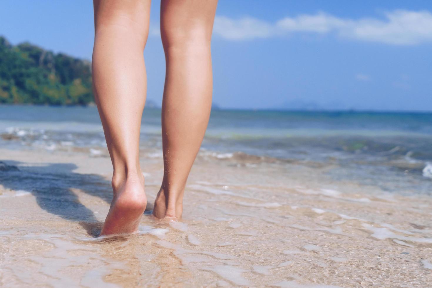 pés de mulher caminhando lentamente na praia tropical de areia foto