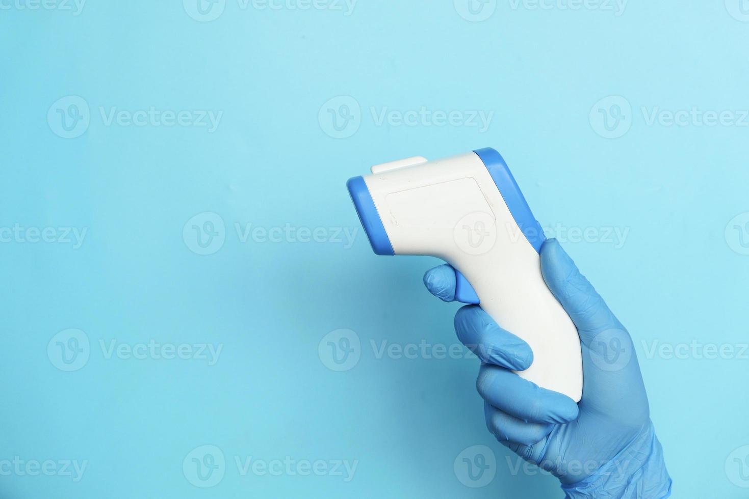 mão segurando termômetro infravermelho em fundo azul foto