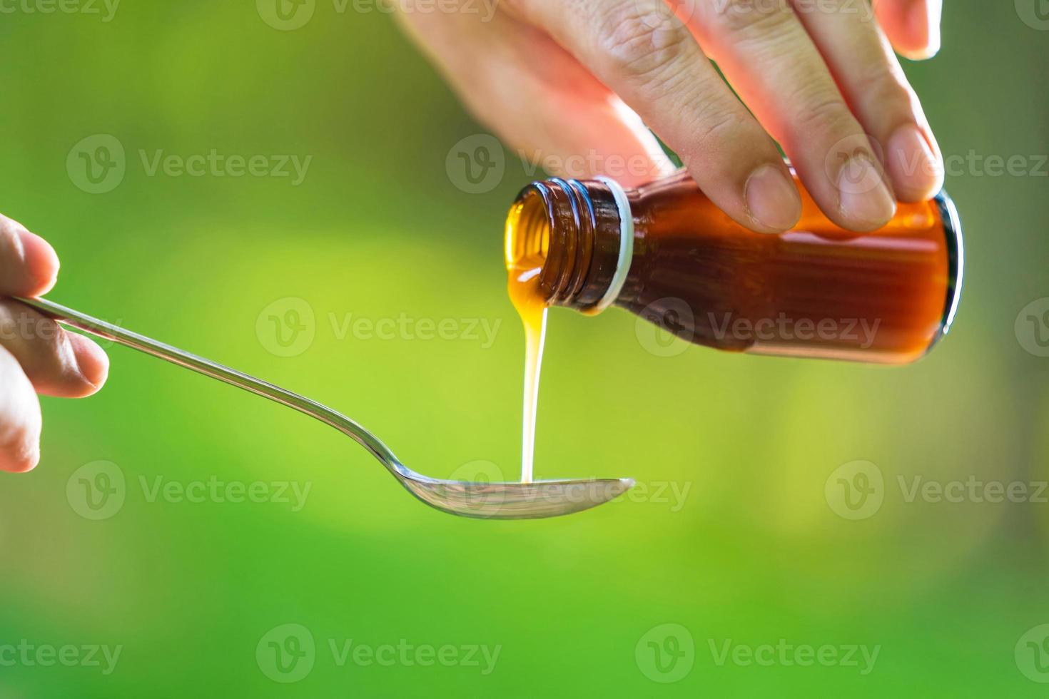 mão do homem derramando medicação ou xarope antipirético da garrafa à colher com fundo natural foto