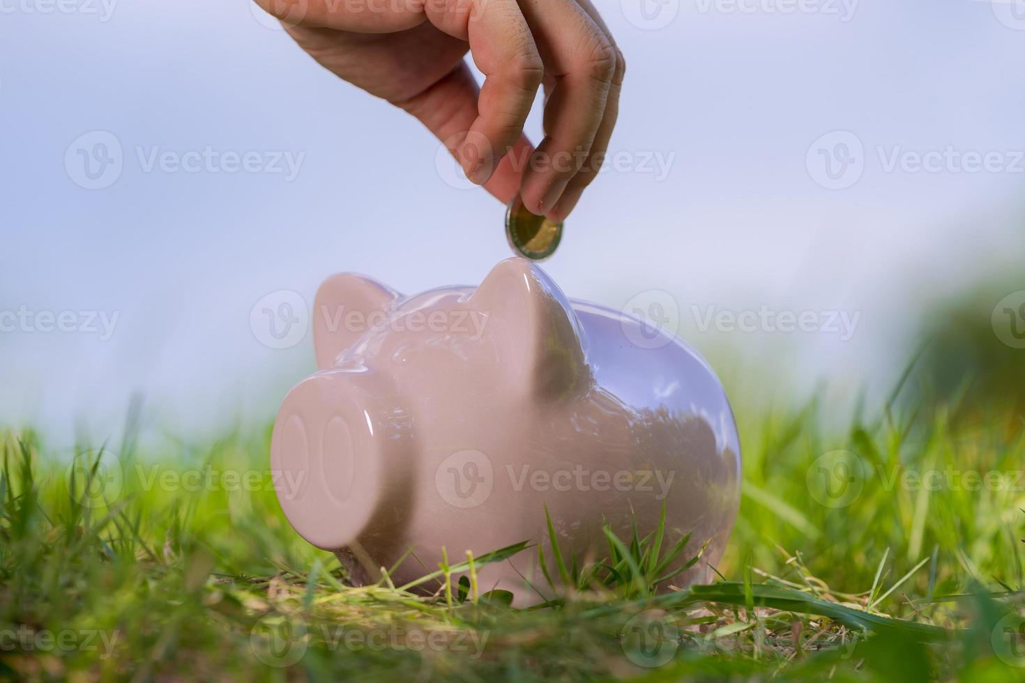 cofrinho rosa na grama com a mão colocando uma moeda foto