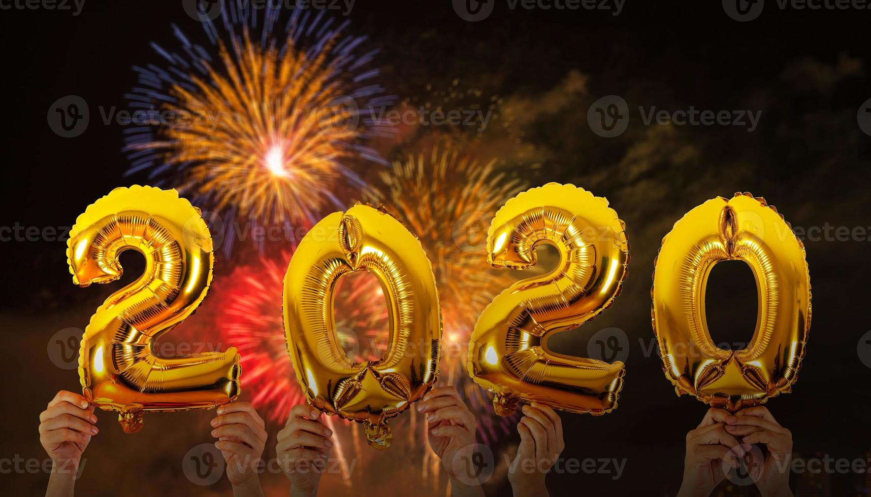 mãos segurando balões com o número 2020 com fundo de fogos de artifício foto