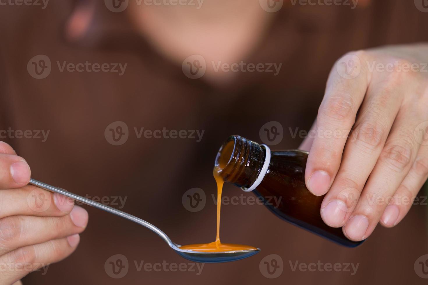 mão do homem derramando medicação ou xarope antipirético da garrafa à colher foto