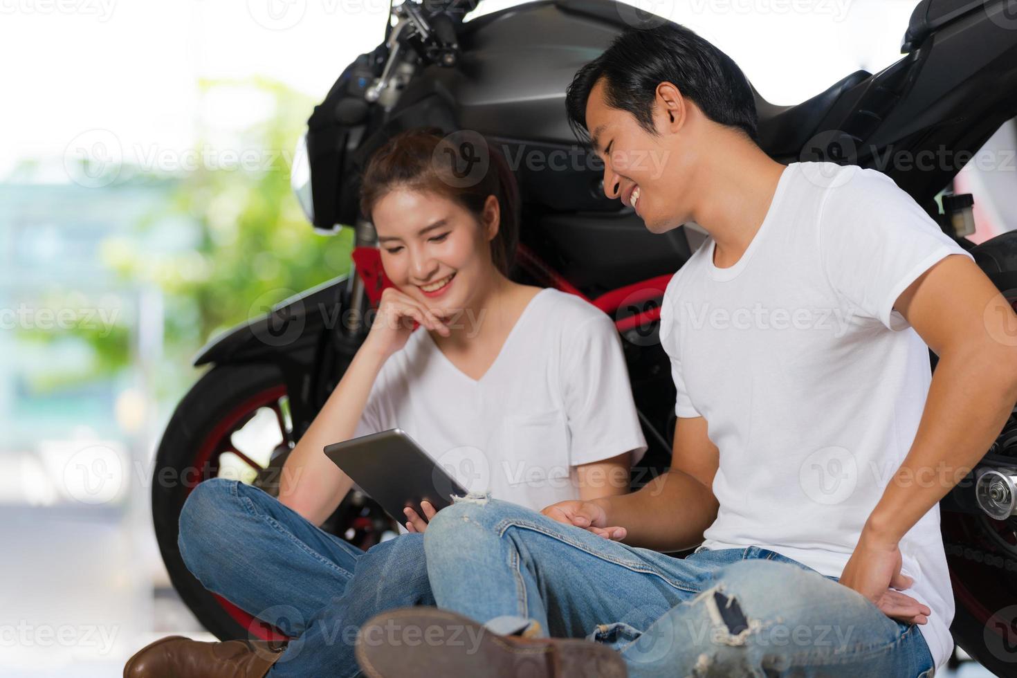 casal feliz usando tablet digital em casa com um fundo de motocicleta foto