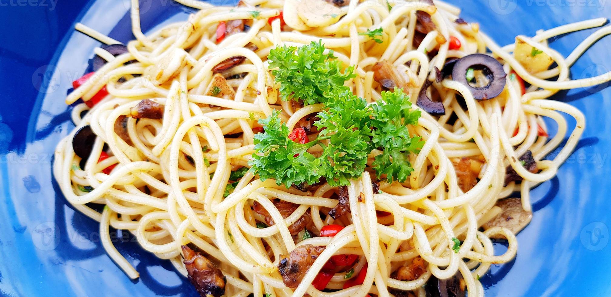 fechar acima quente picante espaguete com mexilhão e cogumelo fatiado ou italiano frutos do mar massa e salsinha ou verde erva em topo dentro azul prato. foto