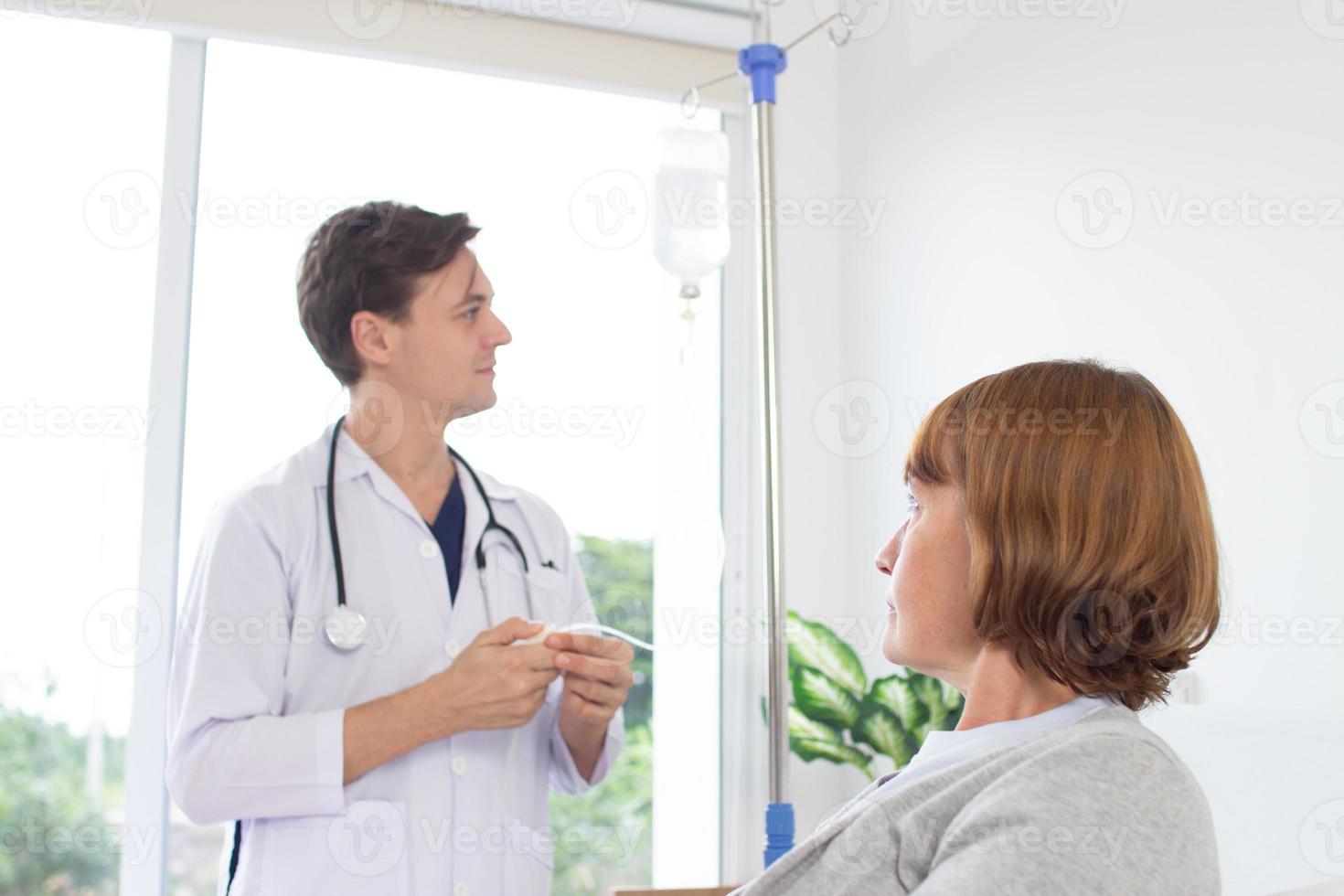 a médico é examinando a paciente dentro a hospital. caucasiano médico vestindo vestido e estetoscópio olhando às normal salina com uma fêmea paciente às a hospital. foto