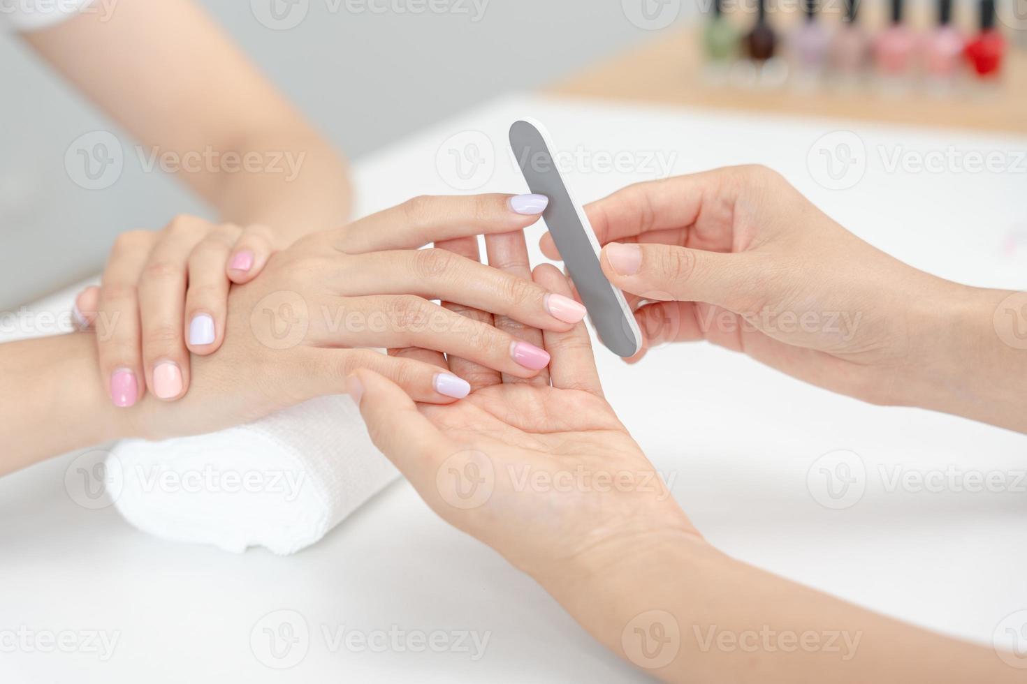 mulher recebe serviço de atendimento por manicure esteticista profissional no centro de spa. salão de beleza de unhas usa lixa de unha para tratamento de esmalte. manicure faz cliente de unha bonita. tratamento de spa para cuidados com o corpo foto