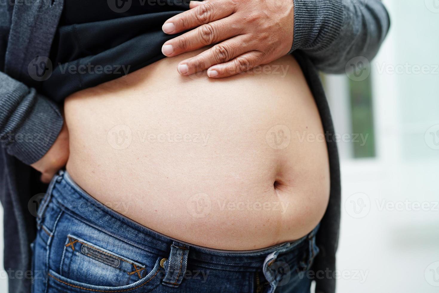 a mulher asiática com excesso de peso usa a mão para espremer a barriga gorda, o sobrepeso e a obesidade. foto