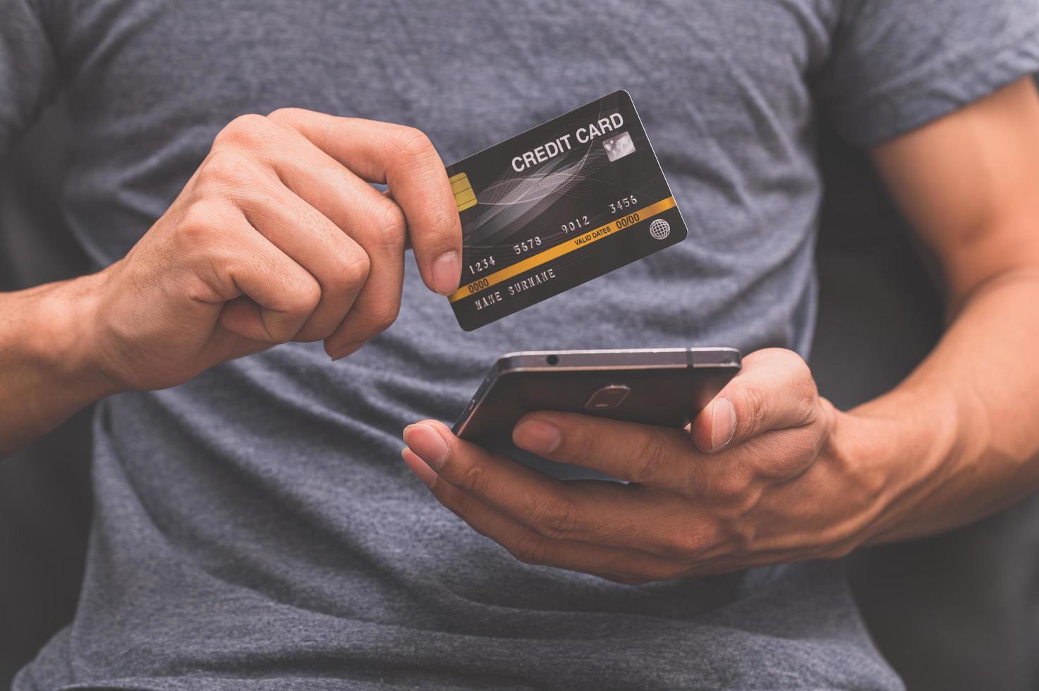 homem segurando um cartão de crédito e usando o smartphone para fazer compras online foto