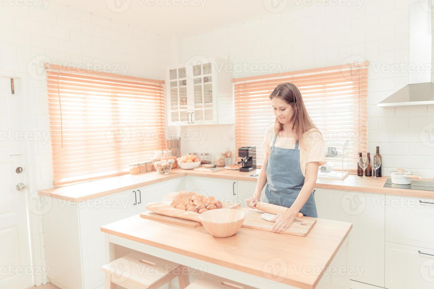 jovem mulher trabalhos com de madeira rolo PIN fazer doce torta ou pastelaria massa dentro cozinha, feliz milenar fêmea amoroso culinária. caloroso tom. foto