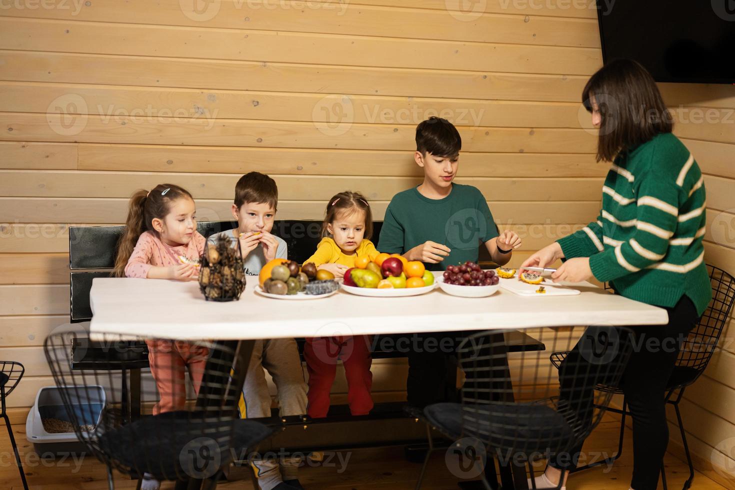 mãe com quatro crianças comer frutas dentro de madeira país casa em fim de semana. mãe cortes a amarelo Dragão fruta. foto