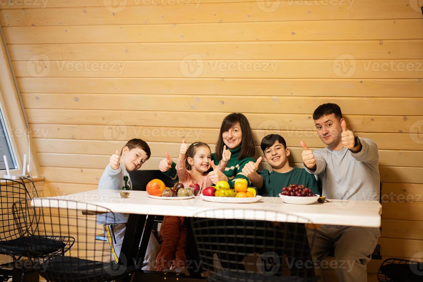 família com três crianças comer frutas dentro de madeira país casa em final de semana e mostra polegar acima. foto