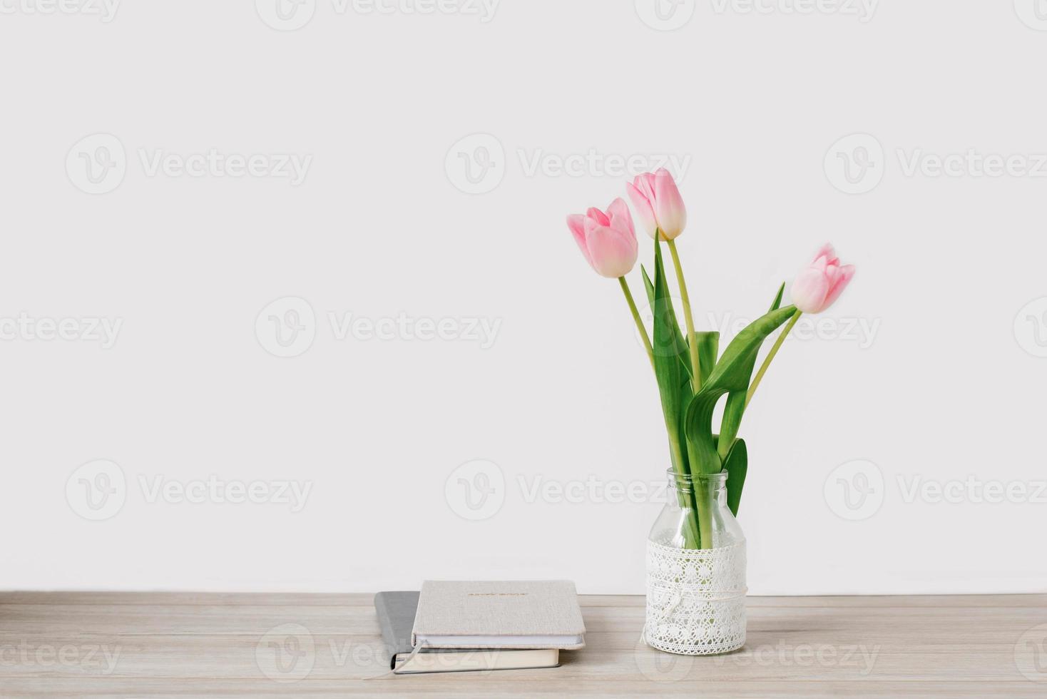 uma ramalhete do Rosa tulipas do Primavera flores dentro uma vaso carrinhos em a Área de Trabalho perto a cadernos. cópia de espaço foto
