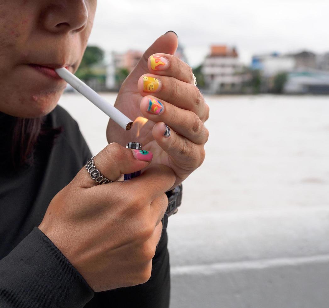 retrato mulher menina adolescente jovem Ásia 1 pessoa vestindo uma chapéu e grandes Preto cabelo vestindo uma Preto camisa mão aguarde fumar cigarro branco cor em pé ao ar livre de a parede ao ar livre foto