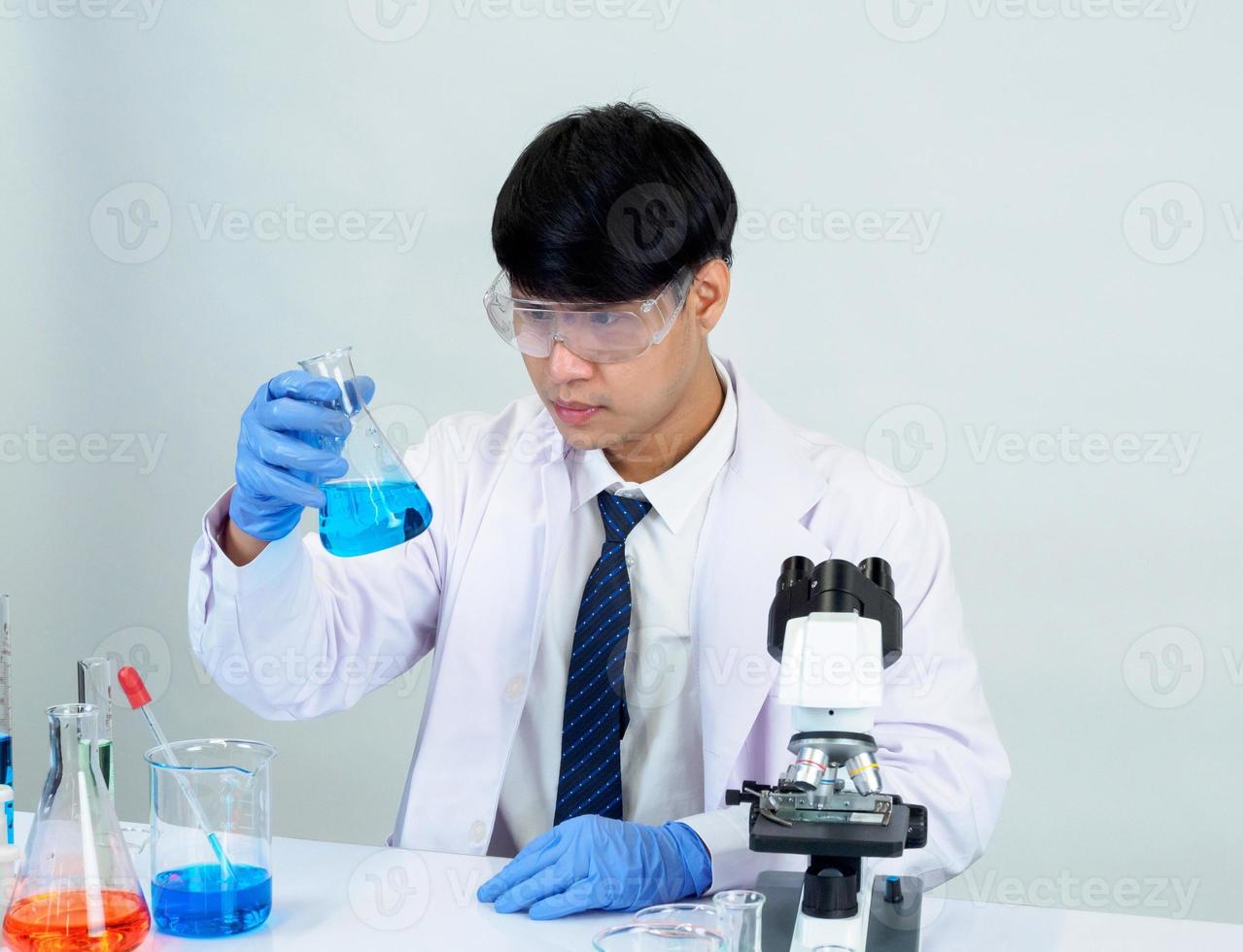 cientista estudante asiático no laboratório de mistura de reagentes em um laboratório de pesquisa científica com tubos de ensaio de vários tamanhos e microscópios. em cima da mesa no fundo branco do laboratório de química de laboratório. foto