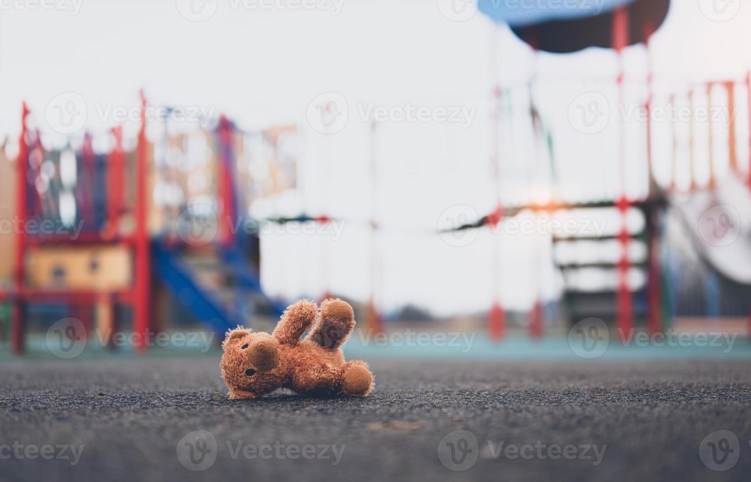 perdido Urso de pelúcia Urso brinquedo deitado não em Parque infantil chão dentro sombrio dia, solitário e triste Castanho Urso boneca mentiu baixa sozinho dentro a parque, perdido brinquedo ou solidão conceito, internacional ausência de crianças dia foto