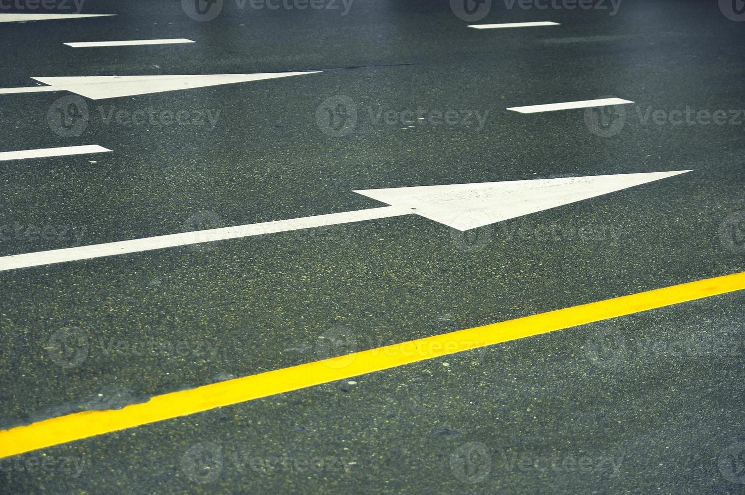 branco Setas; flechas e amarelo linhas em uma molhado asfalto estrada. foto