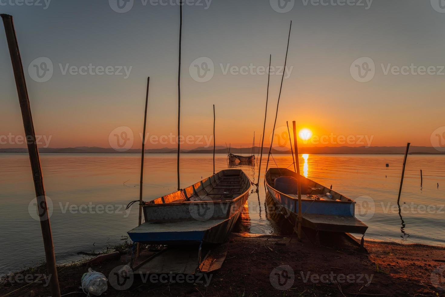 dois pequeno barcos ancorado em a costa do a lago. às pôr do sol foto