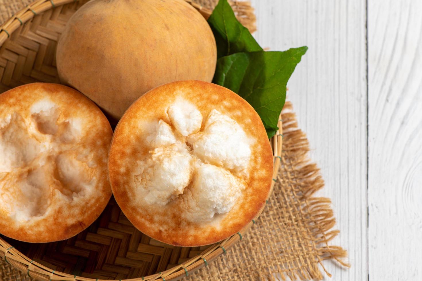 topo Visão do fresco santol frutas em bambu cesta e em branco madeira fundo, foto