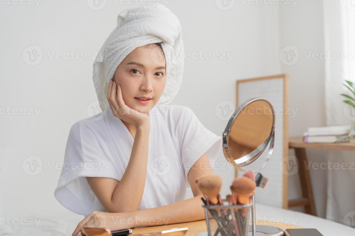 feliz beleza blogueiro conceito, atraente ásia jovem mulher, menina sorrir faço acima face de aplicando escova corar em dela bochecha, olhando dentro a espelho em mesa às lar. pessoas Veja com natural moda estilo foto