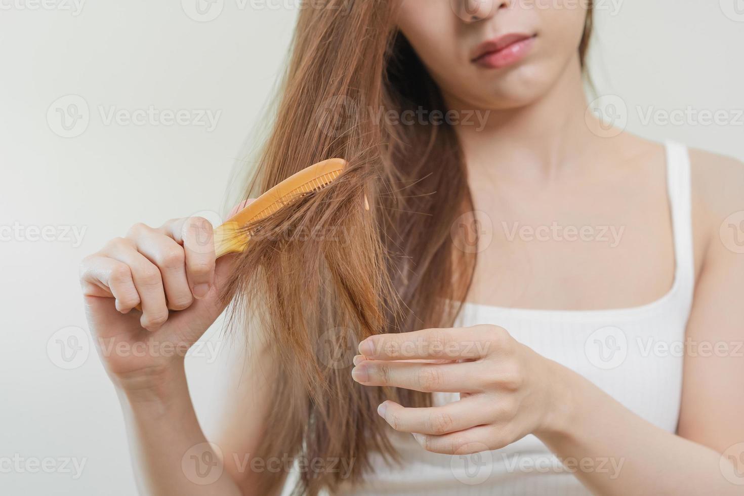 estragado cabelo, frustrado ásia jovem mulher, menina mão dentro segurando escova divisão termina bagunçado enquanto pentear cabelo, não escovado seco grandes cabelo. saúde Cuidado beleza, retrato isolado em branco fundo. foto