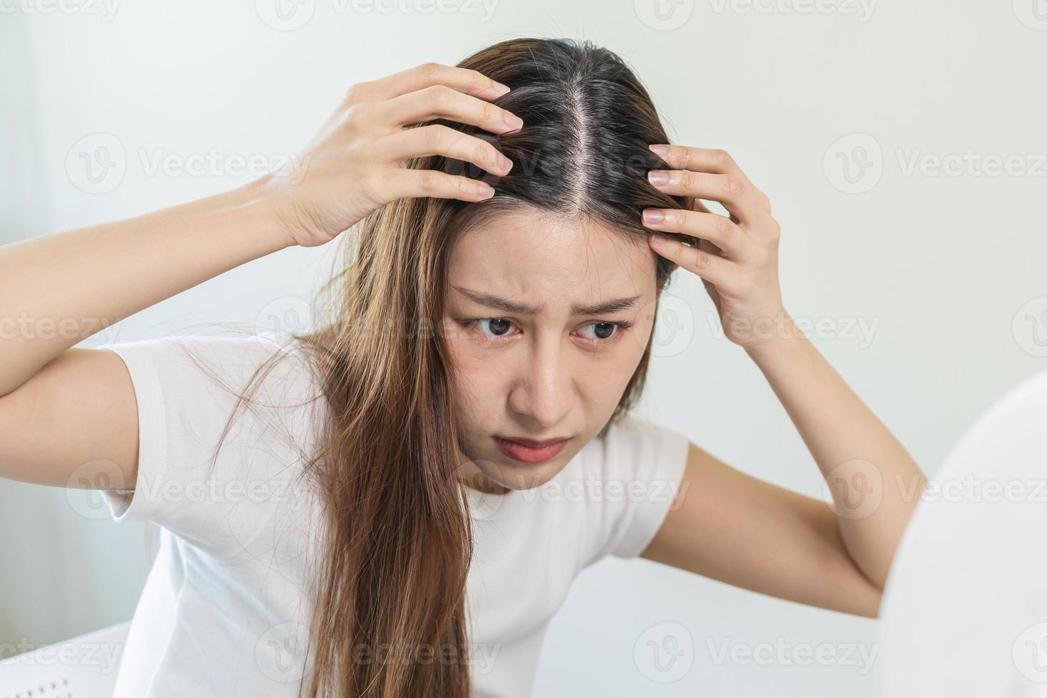 estragado cabelo, face sério ásia jovem mulher preocupação olhando às couro cabeludo dentro espelho, mão dentro pausa para dentro frente cabelo perda, fino problema sintoma às lar. saúde Cuidado xampu beleza, isolado em fundo. foto