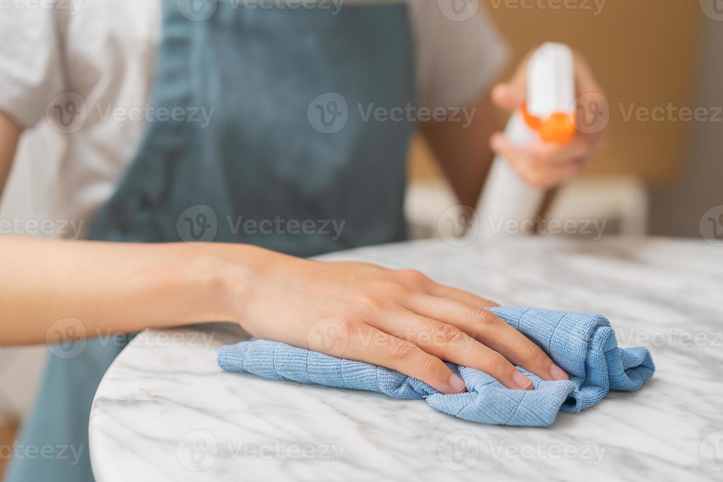 limpeza higiene, ásia jovem empregada mulher, menina mão dentro usando uma água pulverizador garrafa para limpar limpar, usar azul trapo limpando para poeira em branco mármore mesa dentro restaurante. serviço de limpeza limpar, limpador. foto