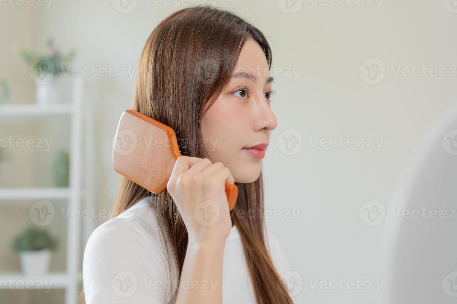 saúde cabelo Cuidado, beleza Maquiagem ásia mulher, menina segurando escova de cabelo e escovar, pentear dela grandes em linha reta cabelo olhando às reflexão dentro espelho dentro manhã rotina depois de salão tratamento, Penteado. foto