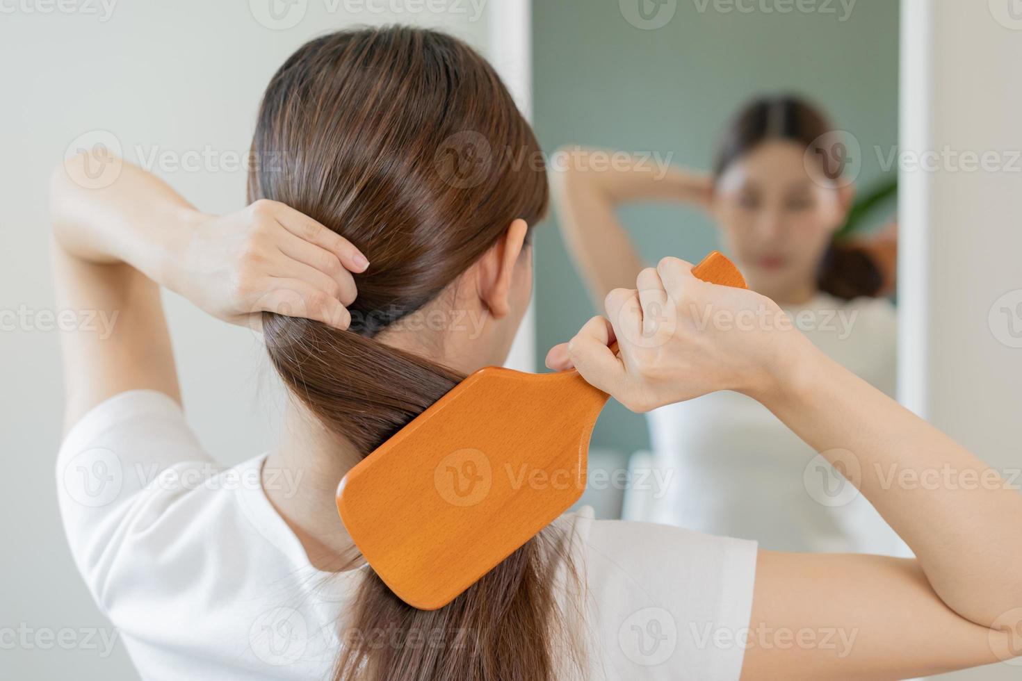 saúde cabelo Cuidado, beleza Maquiagem ásia mulher, menina segurando escova de cabelo e escovar, pentear dela grandes em linha reta cabelo olhando às reflexão dentro espelho dentro manhã rotina depois de salão tratamento, Penteado. foto