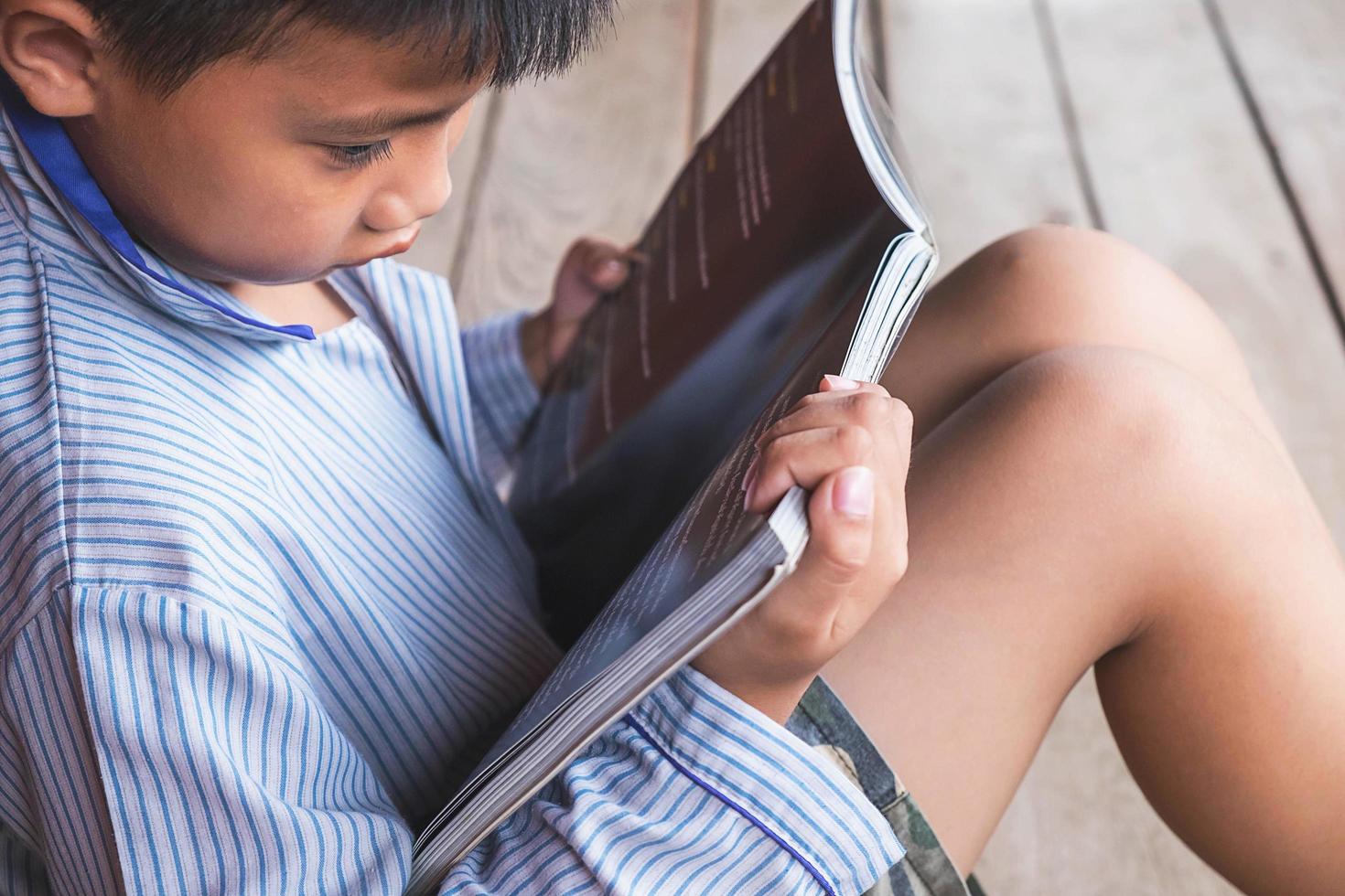 menino sentado lendo um livro no chão de madeira foto