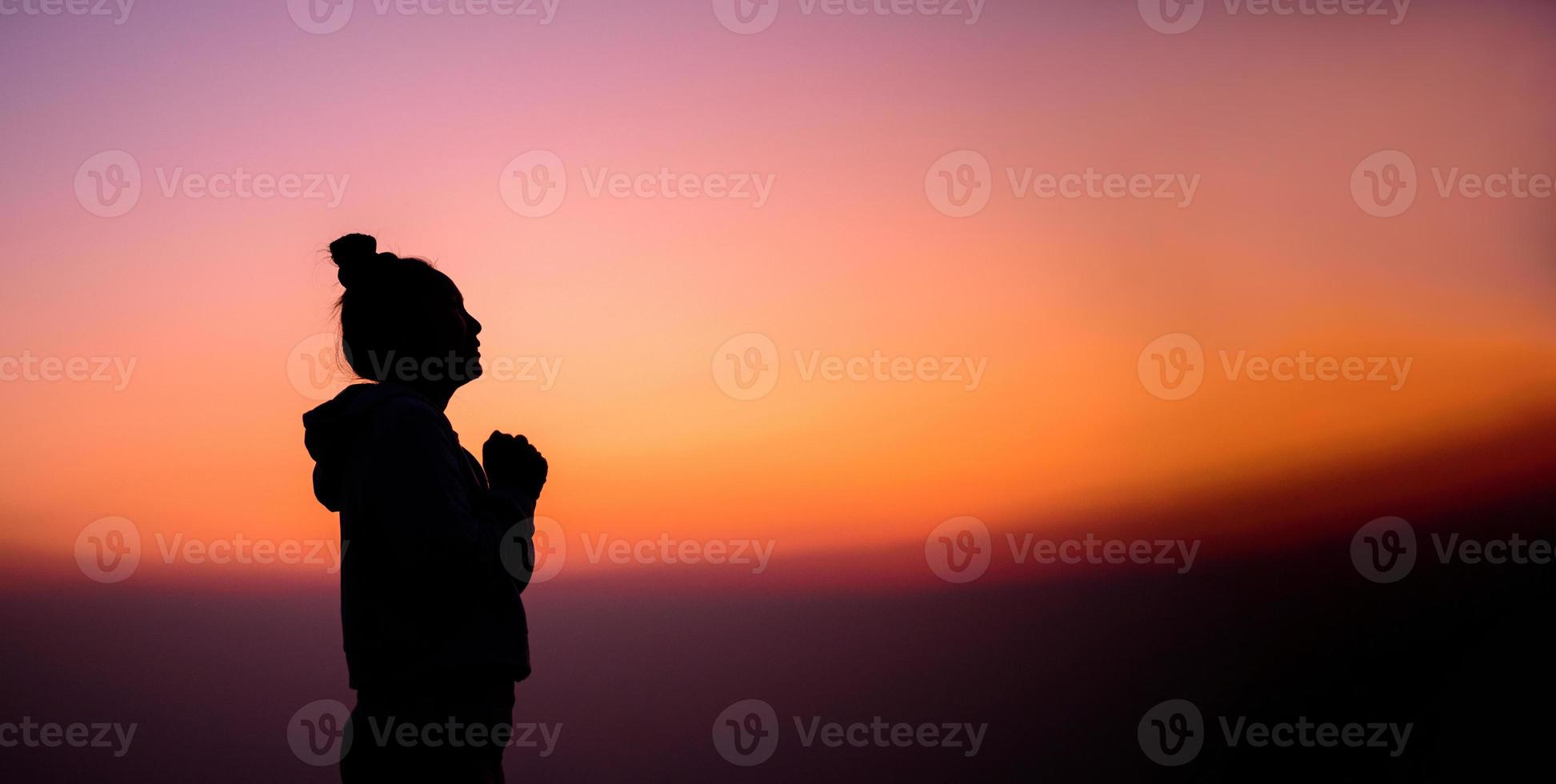 silhueta do lado Visão retrato do uma mulher Rezar e olhando acima às pôr do sol foto