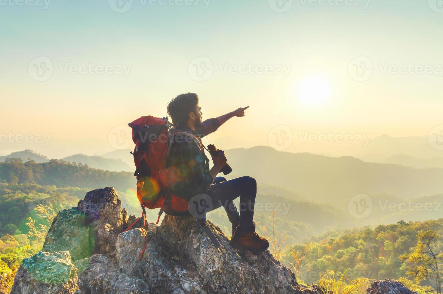 viajante com mochila e segurando binocular sentado em topo do montanha apontando às Visão foto