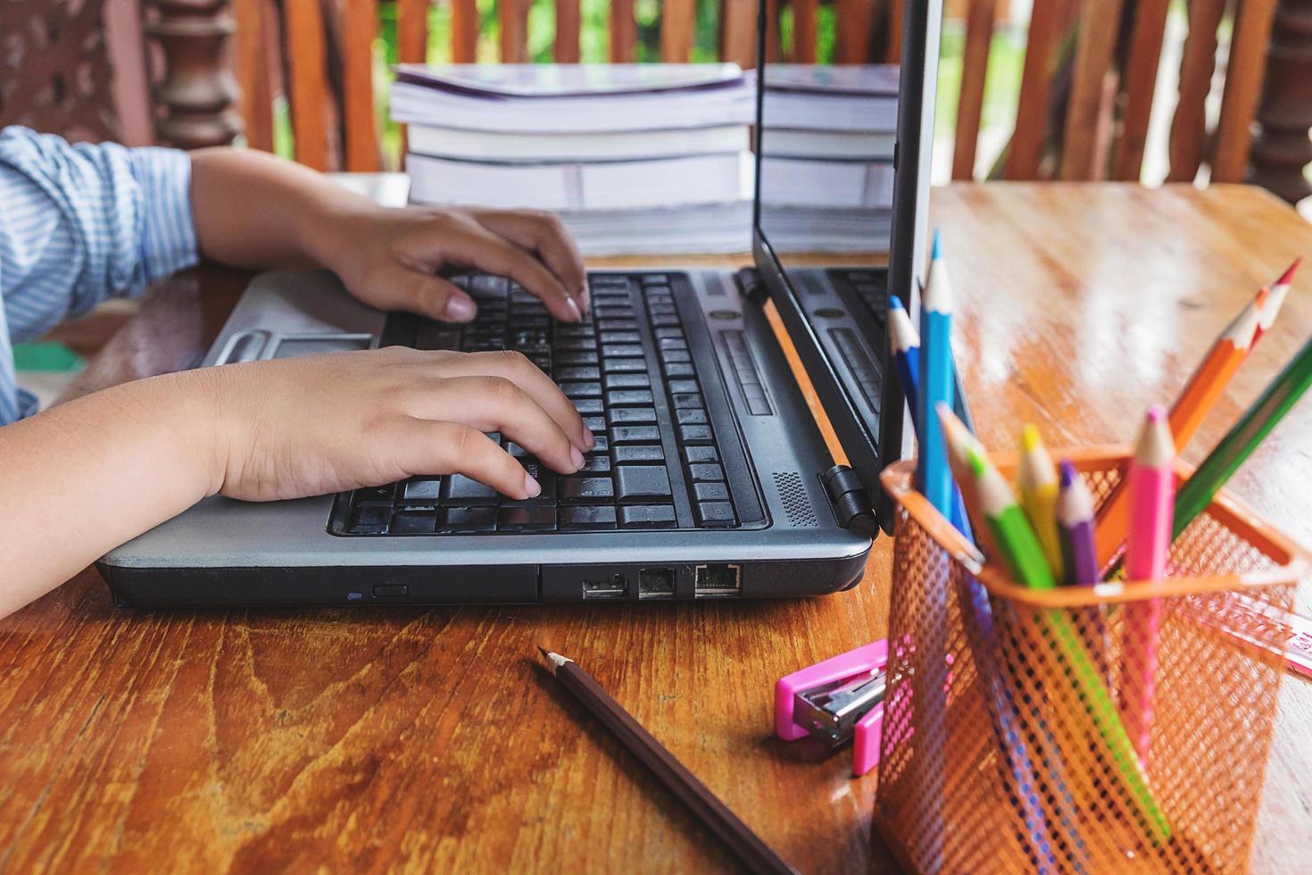 menino trabalhando em um laptop ao lado de um copo de lápis sobre uma mesa de madeira foto