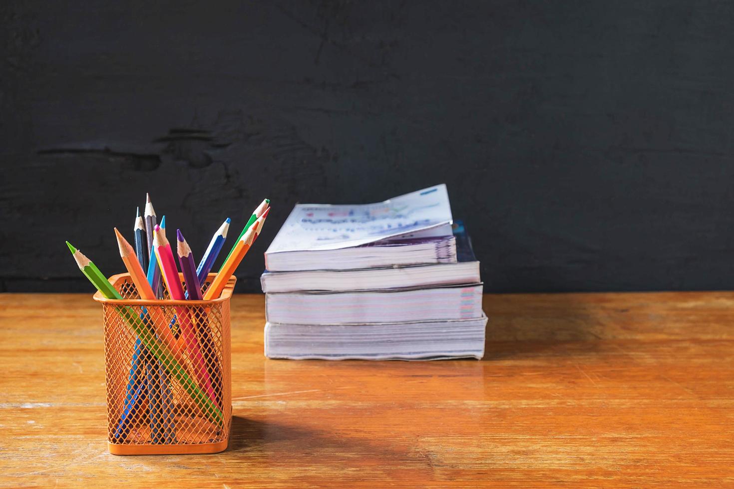 copo de lápis e uma pilha de livros em uma mesa de madeira ao lado de uma parede preta foto